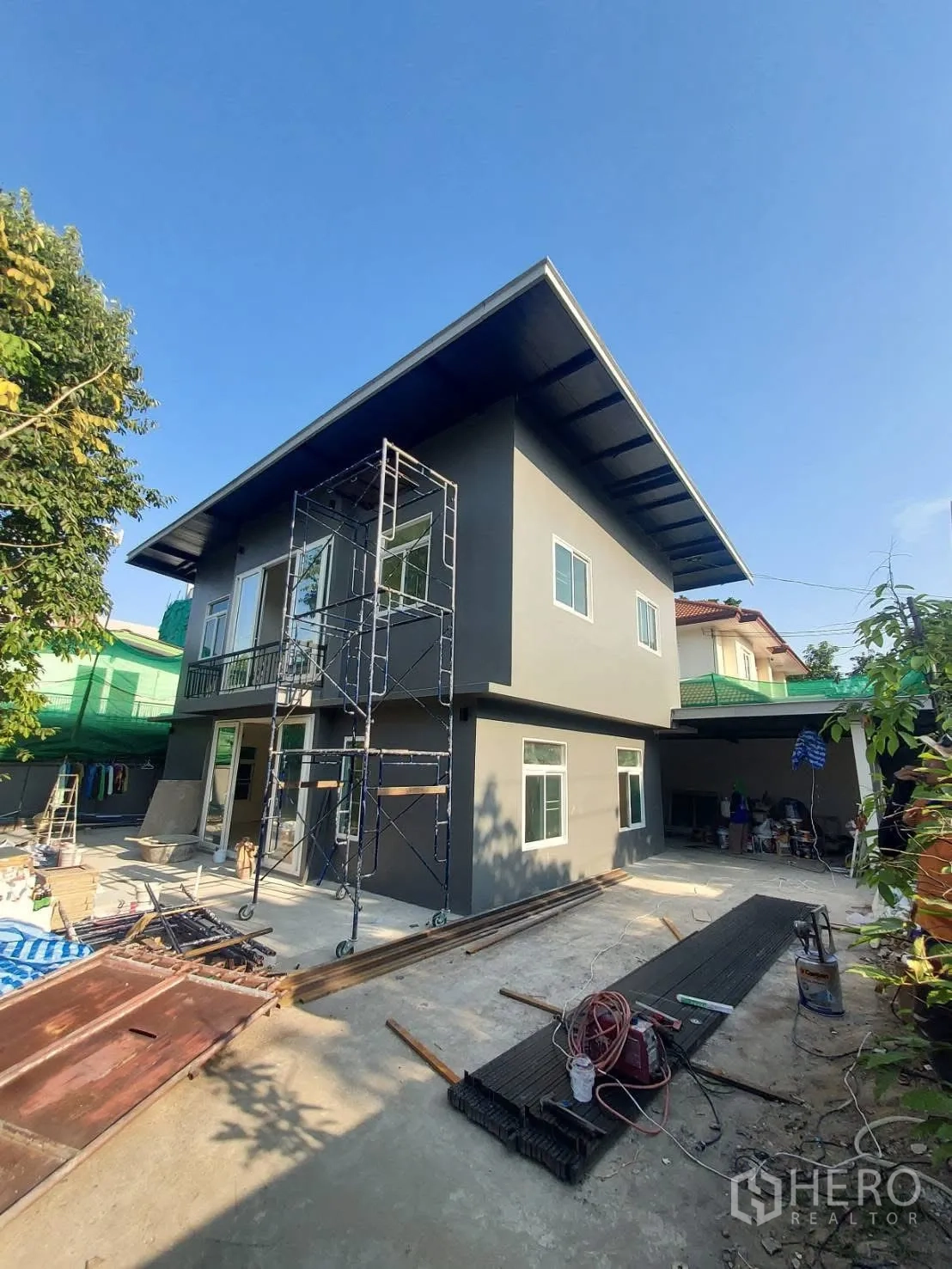 Detached House for rent in Watthana, Bangkok - Modern two-storey gray house exterior with wide eaves, scaffolding and a paved yard.