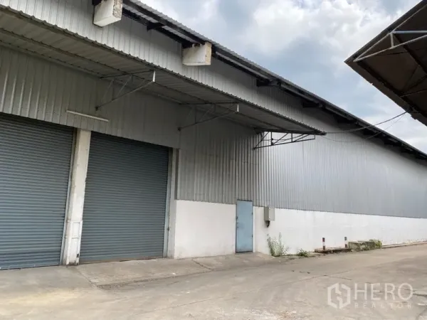 货栈 出租在Khlong Luang, Pathum Thani - 金属板外墙仓库外观，配有两扇大型卷帘门和带顶装卸区。