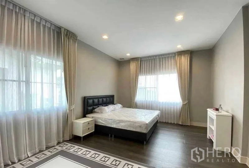 Detached House for rent in Bang Khen, Bangkok - Guest bedroom with dark bedframe, wood floors and soft curtains.