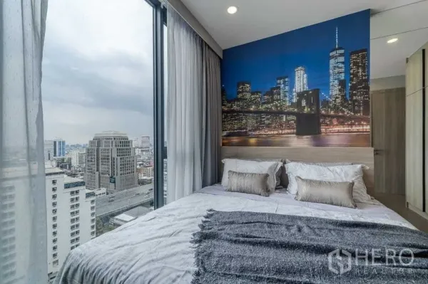 คอนโด ให้เช่าในPathum Wan, Bangkok - ห้องนอนมุมกระจก พื้นถึงฝ้า วิวสกายไลน์ พร้อมวอลเปเปอร์เมืองยามค่ำคืนหลังเตียง