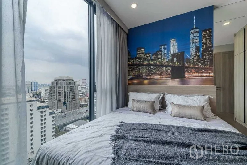 คอนโด ให้เช่าในPathum Wan, Bangkok - ห้องนอนมุมกระจก พื้นถึงฝ้า วิวสกายไลน์ พร้อมวอลเปเปอร์เมืองยามค่ำคืนหลังเตียง