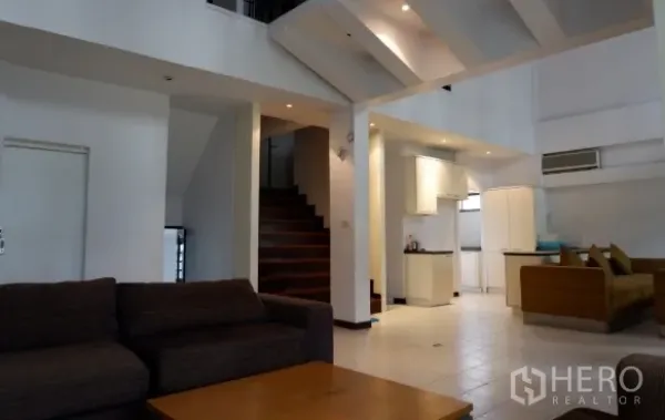 Townhouse for sale in Khlong Toei, Bangkok - Open-plan living and kitchen area with double-height ceiling, recessed lights and staircase.