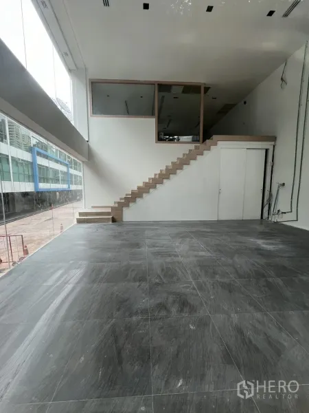 零售空间 出租在Khlong Toei, Bangkok - 双层挑高零售室内，灰色地砖、木楼梯与夹层，街边落地玻璃。