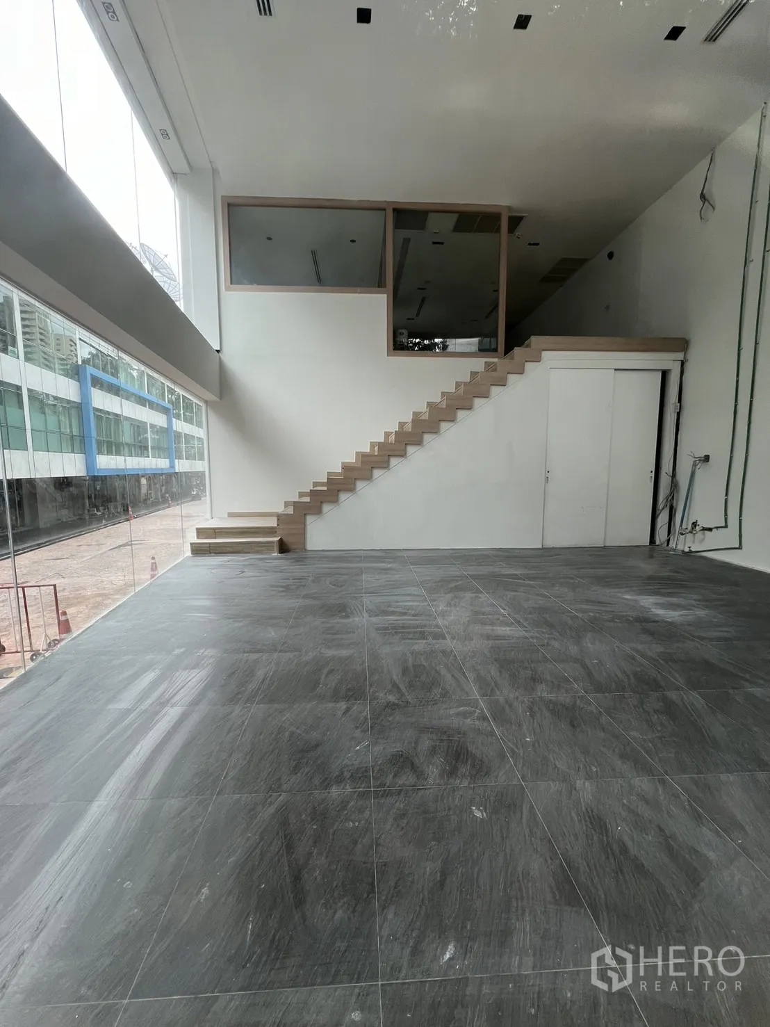 零售空间 出租在Khlong Toei, Bangkok - 双层挑高零售室内，灰色地砖、木楼梯与夹层，街边落地玻璃。
