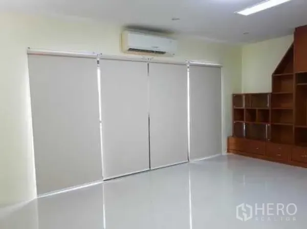 Townhouse for rent in Khlong Toei, Bangkok - Living area with roller blinds, built-in wooden shelving and a wall-mounted air conditioner.