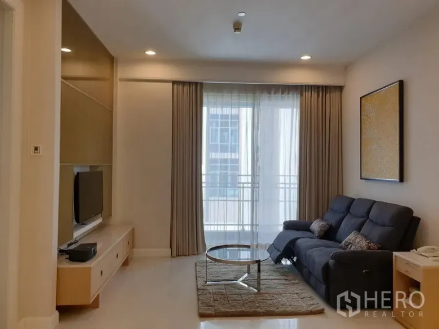 Condominium for rent in Pathum Wan, Bangkok - Cozy living room with sofa, round coffee table and sliding doors to a small balcony.