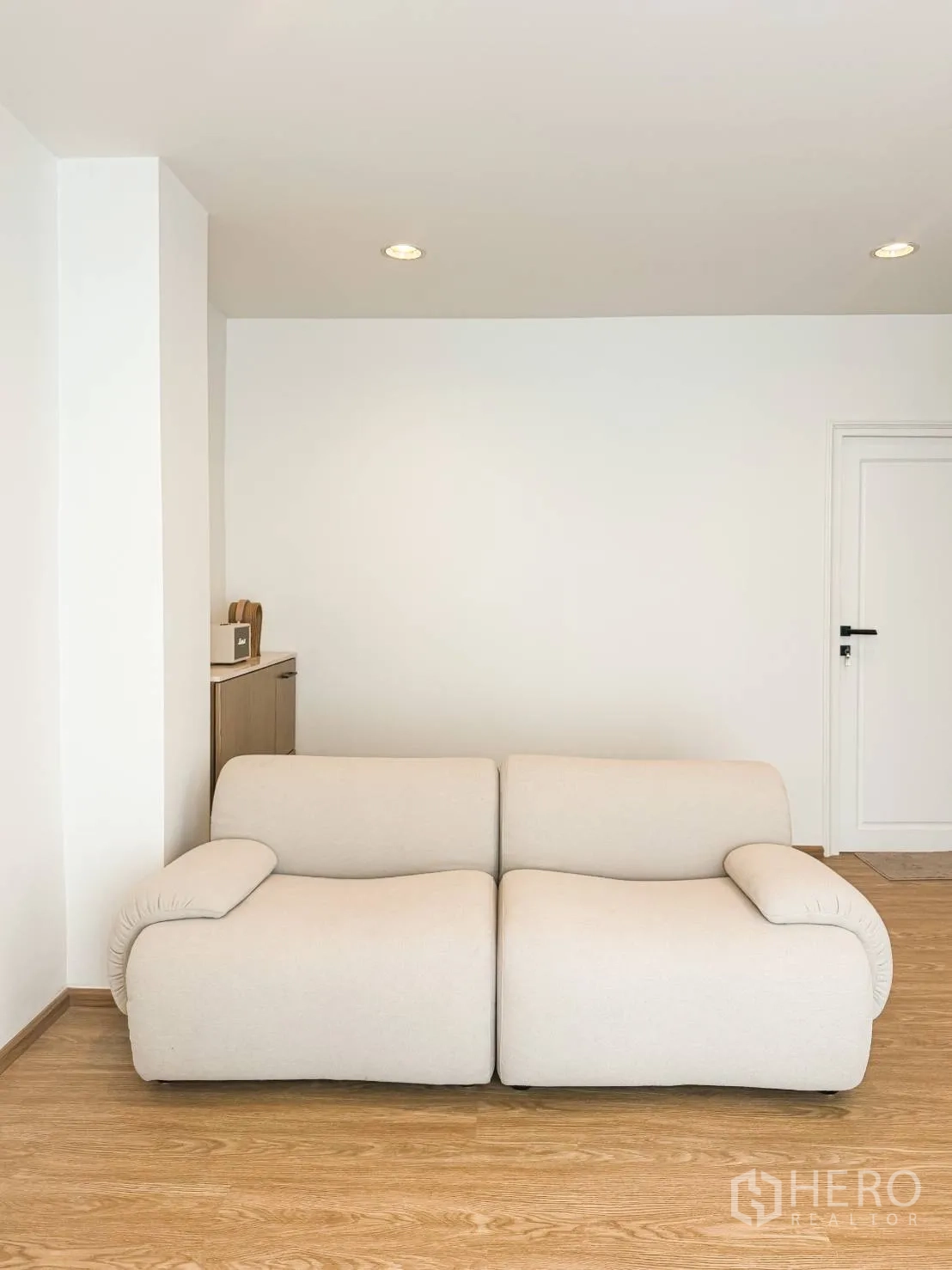 Shophouse for sale in Watthana, Bangkok - Minimalist lounge with a cream two-seater sofa on wood flooring and white walls.