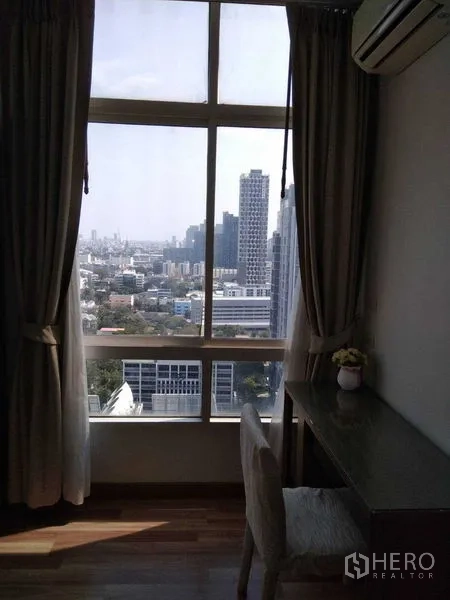 Condominium for rent in Watthana, Bangkok - Work desk by floor-to-ceiling window with skyline view and curtains.