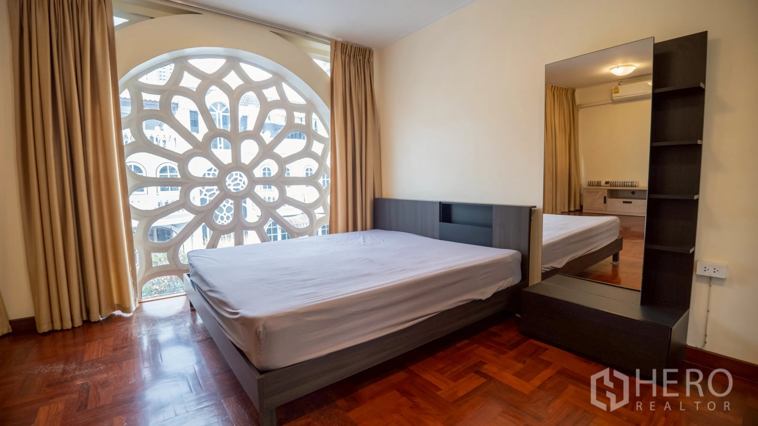 Townhouse for rent in Khlong Toei, Bangkok - Bedroom with bed beside a large circular patterned window and full-length mirror.