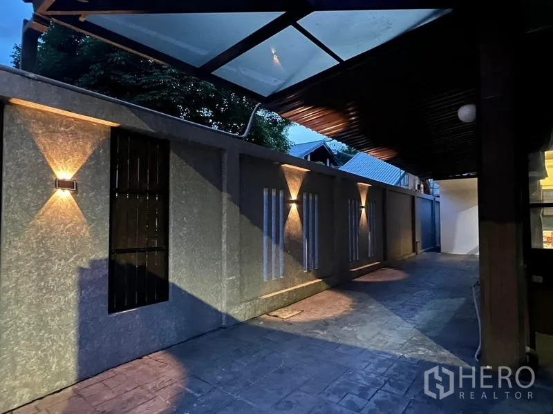 Townhouse for rent in Phaya Thai, Bangkok - Side walkway at dusk with wall sconces and canopy roof lighting the entrance.
