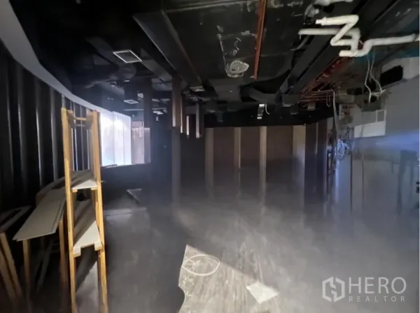 零售空间 出租 - 未装修的零售室内，黑色裸顶可见风管与管线，侧边有搁架，带弧形临街窗线，适合二次装修。