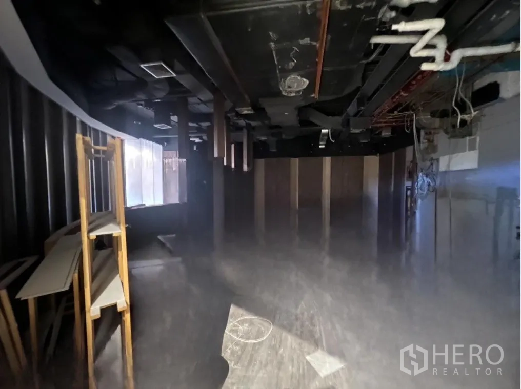 零售空间 出租 - 未装修的零售室内，黑色裸顶可见风管与管线，侧边有搁架，带弧形临街窗线，适合二次装修。