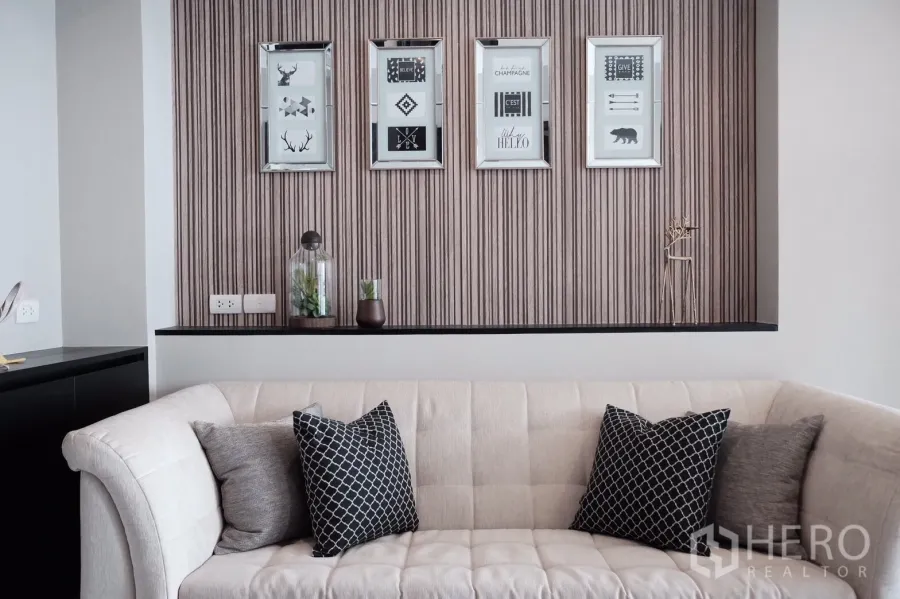 คอนโด ให้เช่าหรือขายในKhlong Toei, Bangkok - ห้องนั่งเล่นสไตล์โมเดิร์น โซฟาสีครีม หมอนลายกราฟิก และกรอบภาพบนผนังลายเส้น
