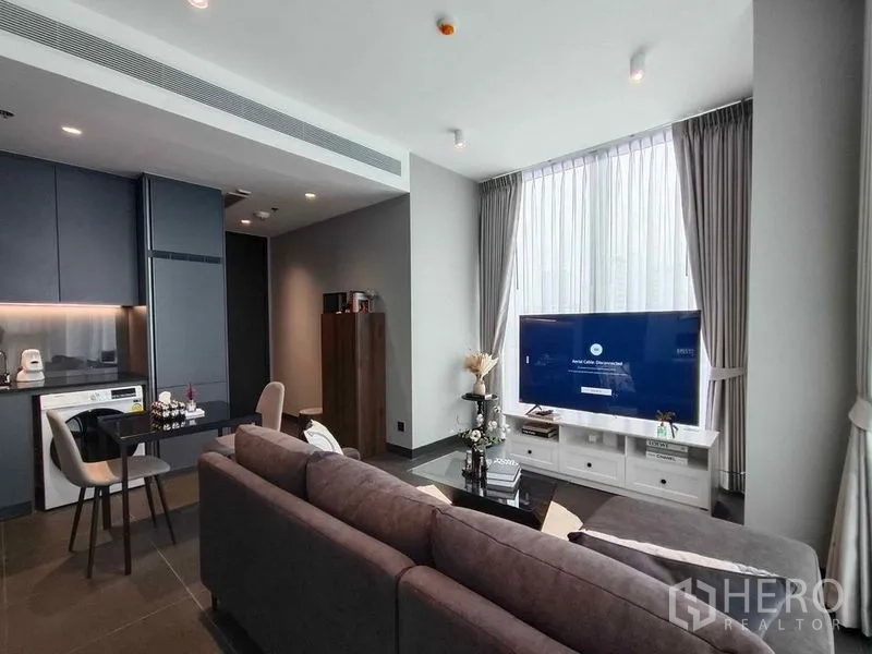 Condominium for rent in Bang Rak, Bangkok - Open-plan living beside a sleek kitchenette with accent lighting and a large TV by the window.