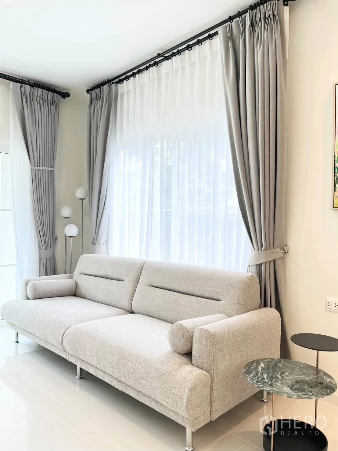 Detached House for rent in Bang Phli, Samut Prakan - Living room corner with light gray sofa, sheer curtains, and round side tables.