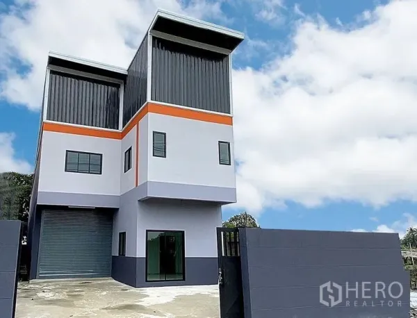 工厂 出租在Bang Bua Thong, Nonthaburi - 现代两层工厂外观，带卷闸门、庭院大门和停车区，位于暖武里邦武通。