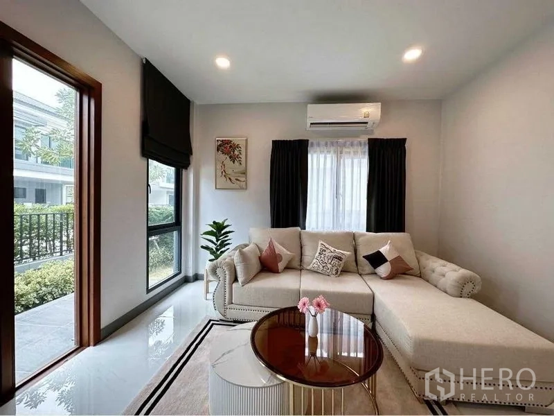 Detached House for rent or sale in Bang Phli, Samut Prakan - Airy living room with L-shaped sofa, round coffee table and large windows.