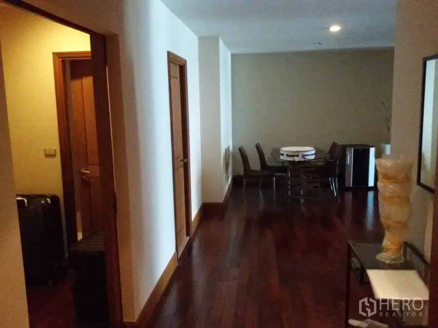 Condominium for rent in Sathon, Bangkok - Wide corridor with dark wooden flooring leading to a glass dining table in a Sathorn condo.