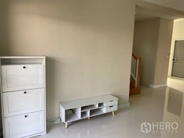 บ้าน ให้เช่าหรือขายในSuan Luang, Bangkok - มุมมินิมอลพร้อมตู้สีขาวและชั้นวางทีวี ต่ำ ข้างโถงบันได