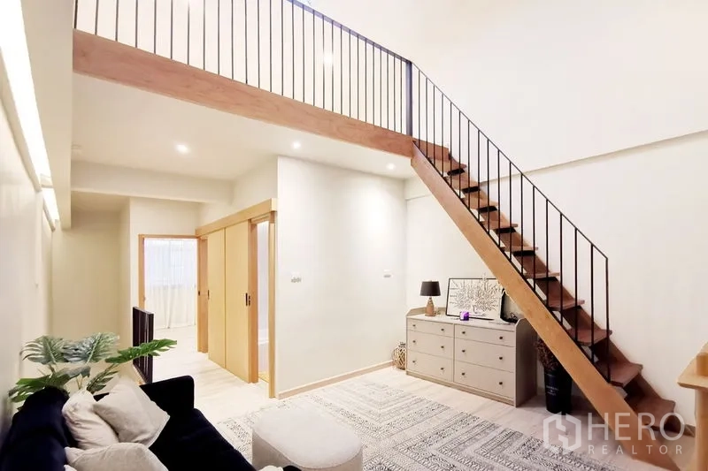 联排别墅 出租在Khlong Toei, Bangkok - 阁楼风客厅，木楼梯、通往房间的推拉门与斗柜。