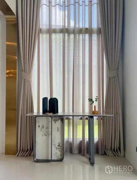 Detached House for rent or sale in Bang Kapi, Bangkok - Tall window with elegant full-length curtains and a slim marble console table.
