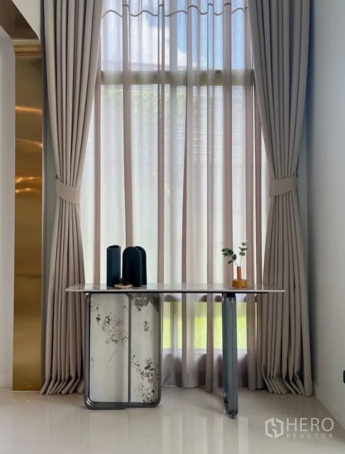 Detached House for rent or sale in Bang Kapi, Bangkok - Tall window with elegant full-length curtains and a slim marble console table.