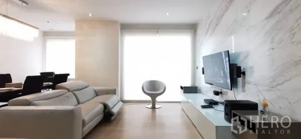 คอนโด ให้เช่าหรือขายในWatthana, Bangkok - โซนรับแขกผนังลายหินอ่อน ทีวีติดผนัง เก้าอี้สีขาว และมู่ลี่กรองแสง