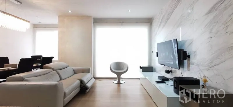 คอนโด ให้เช่าหรือขายในWatthana, Bangkok - โซนรับแขกผนังลายหินอ่อน ทีวีติดผนัง เก้าอี้สีขาว และมู่ลี่กรองแสง