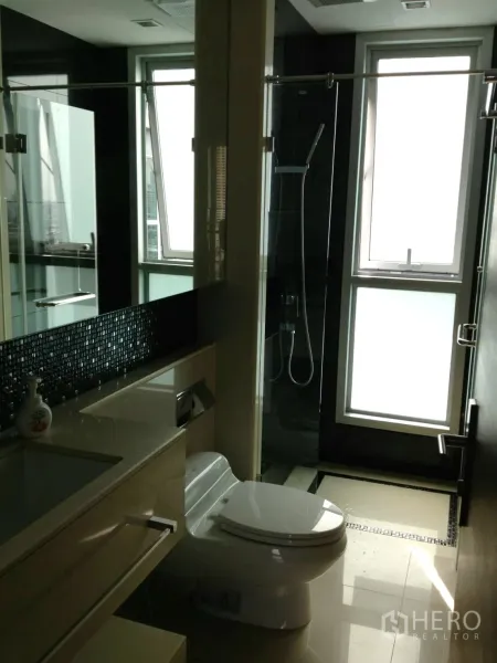 Condominium for rent in Ratchathewi, Bangkok - Modern bathroom featuring a glass shower enclosure, frosted windows, vanity and toilet.