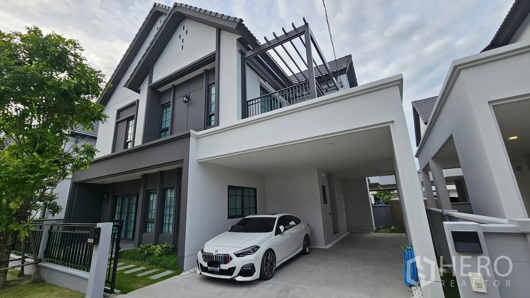 Detached House for rent or sale in Bang Phli, Samut Prakan - Modern two-storey detached house exterior with covered carport, white sedan, balcony pergola and landscaped front yard.
