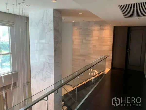 Condominium for rent in Khlong Toei, Bangkok - Stair landing and hallway with glass balustrade, marble accents and tall windows.
