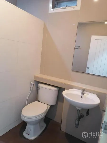 Shophouse for rent in Bang Rak, Bangkok - Compact modern restroom featuring toilet, sink, mirror and neutral wall tiles.