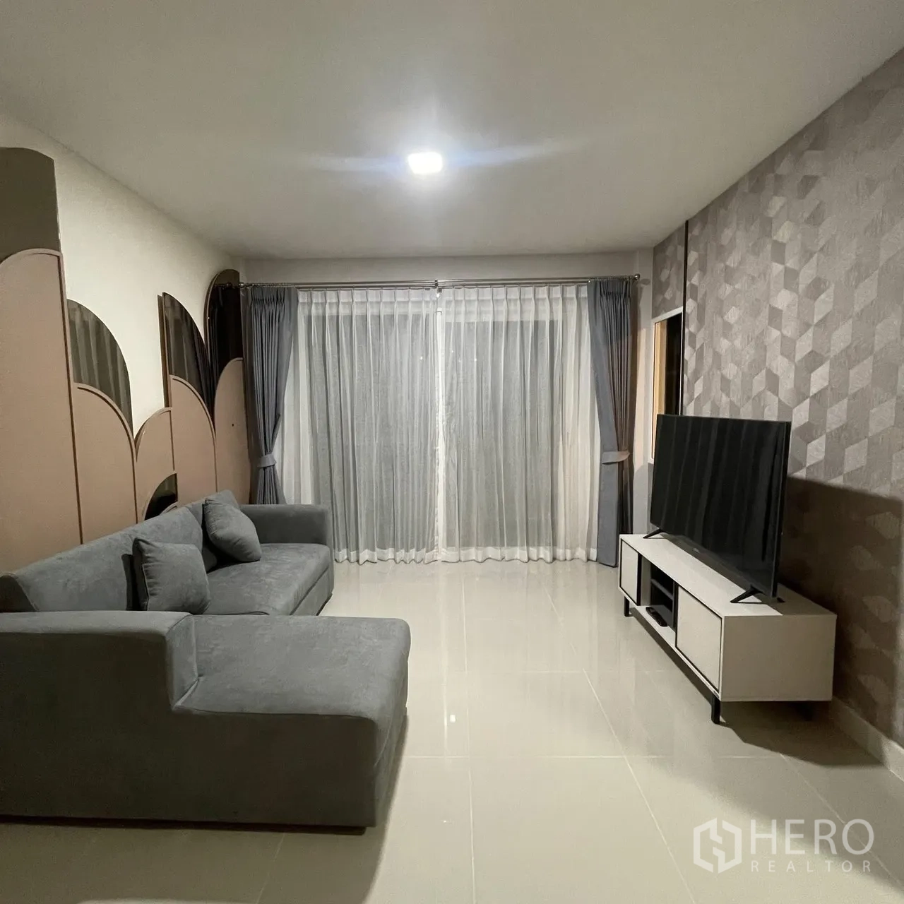 Semi-detached House for rent in Bang Phli, Samut Prakan - Cozy living room with sectional sofa, TV console, feature wall and sliding glass doors with curtains.