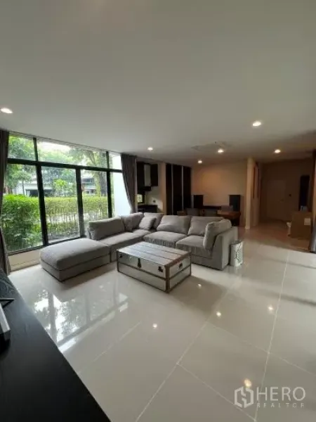 独立式住宅 出租在Bang Kapi, Bangkok - 采光充足的客厅，L型沙发，亮面瓷砖地面，落地窗望花园。