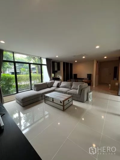 独立式住宅 出租在Bang Kapi, Bangkok - 采光充足的客厅，L型沙发，亮面瓷砖地面，落地窗望花园。