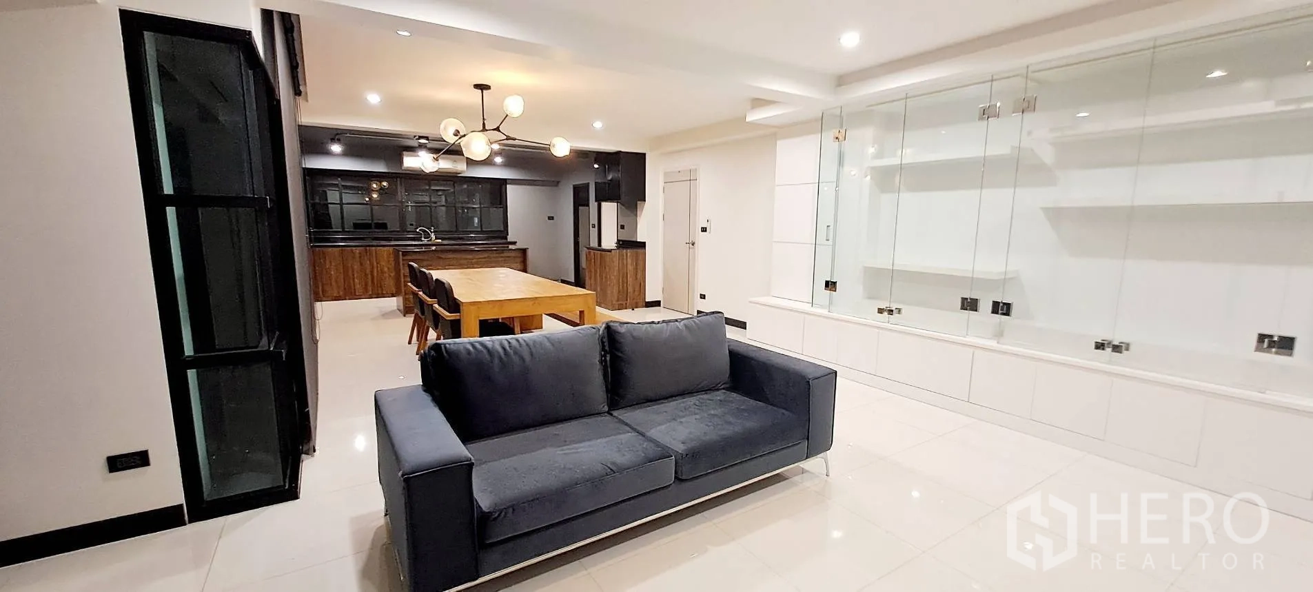 Apartment for rent in Phra Khanong, Bangkok - Bright living room with modern light fixture and white media wall.