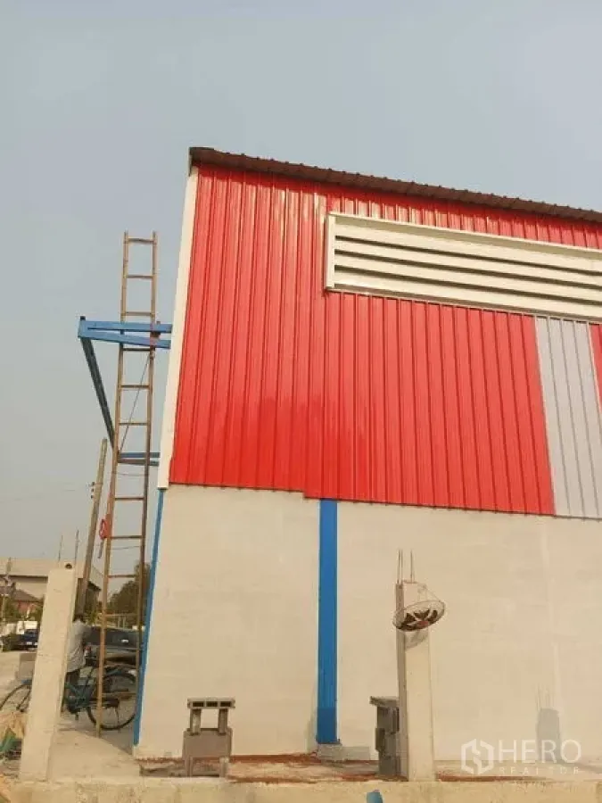 货栈 出租在Pathum Thani - 仓库转角视角，红色金属墙面、通风百叶与混凝土下墙。