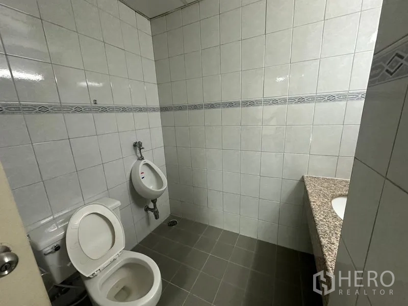 办公空间 出租在Watthana, Bangkok - 办公室卫生间，瓷砖墙地，配坐便器、尿斗与花岗岩台面洗手盆。