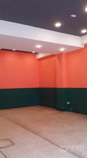 店屋 出租在Bang Khen, Bangkok - 店内角落，橙绿墙面、嵌入式照明与瓷砖地面。