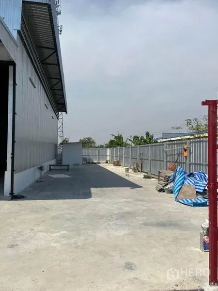 Warehouse for rent in Nonthaburi - Concrete driveway beside a metal-clad warehouse with secure fence and open loading yard in Sai Noi, Nonthaburi.