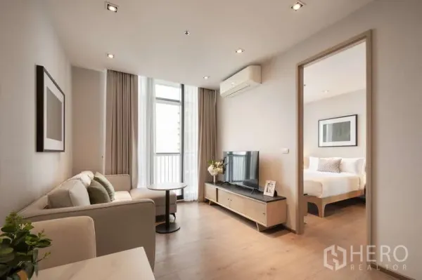 Condominium for rent in Khlong Toei, Bangkok - Bright living room with sofa, TV unit, and floor-to-ceiling windows leading to the bedroom and balcony.