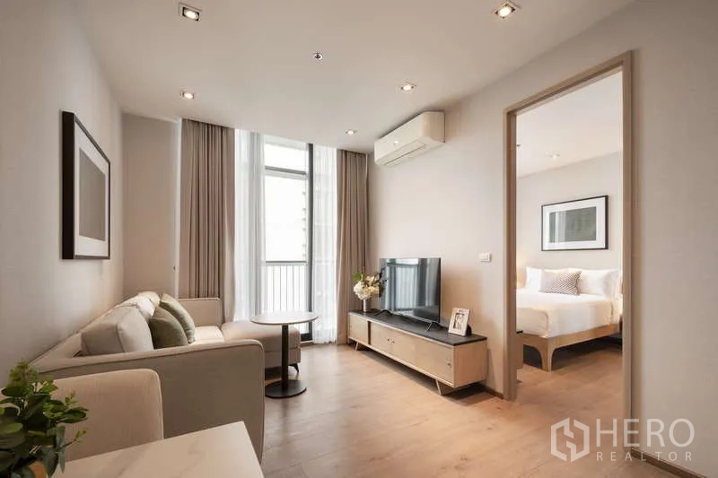 Condominium for rent in Khlong Toei, Bangkok - Bright living room with sofa, TV unit, and floor-to-ceiling windows leading to the bedroom and balcony.
