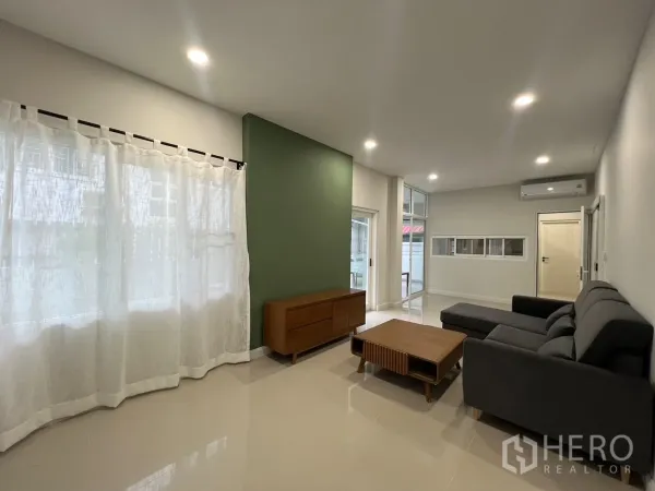 Detached House for rent in Saphan Sung, Bangkok - Bright living room with gray sofa, green accent wall and sheer curtains.