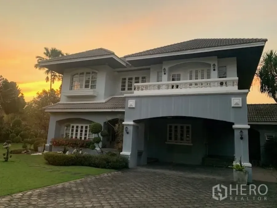 独立式住宅 出租在Khan Na Yao, Bangkok - 两层独栋别墅外观，带有顶棚车位、阳台与大前院，黄昏时分。