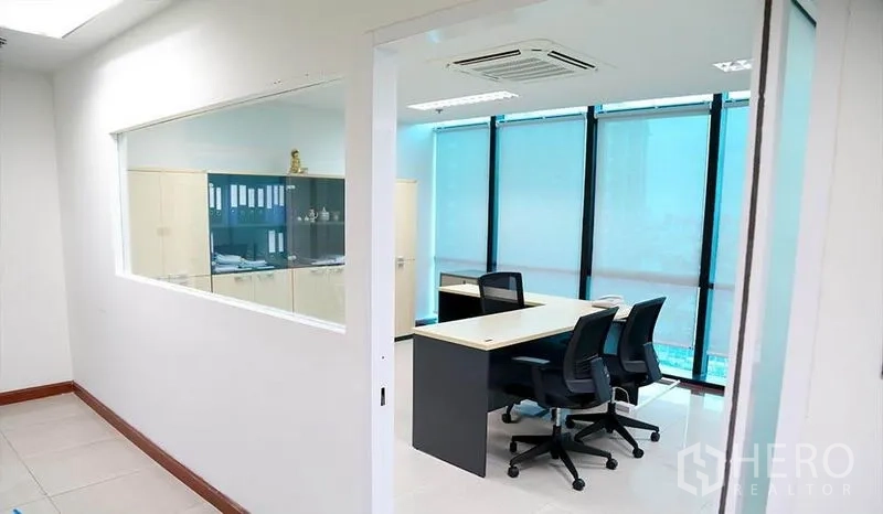 Office Space for rent in Huai Khwang, Bangkok - Glass-partitioned private office with desks beside blue-tinted floor-to-ceiling windows.