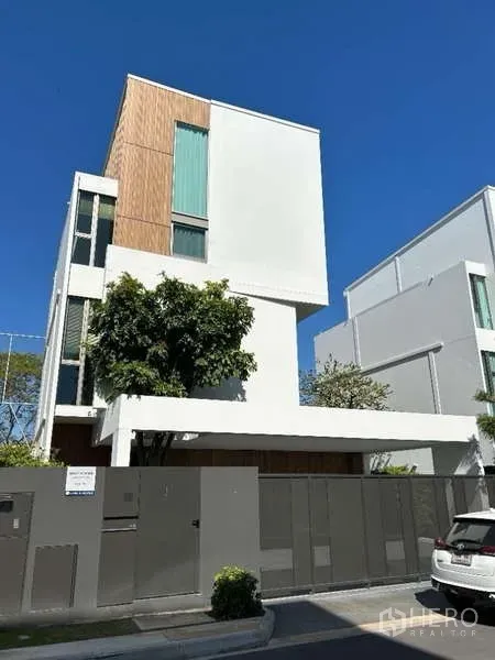 Detached House for rent in Saphan Sung, Bangkok - Modern three-storey detached house with white facade, wood accents and tall windows behind a gated wall.
