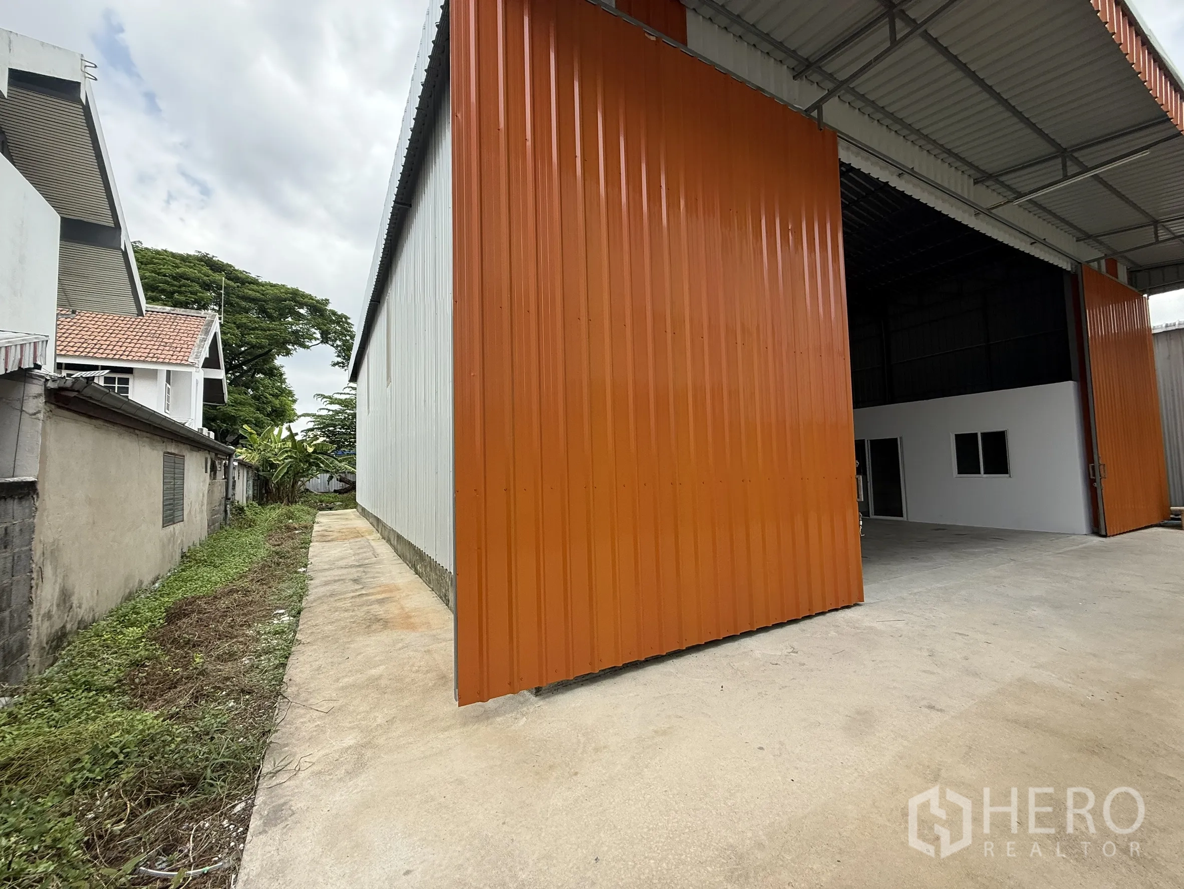 Warehouse for rent in Wang Thonglang, Bangkok - Exterior view of warehouse entrance with large sliding metal door and paved area.
