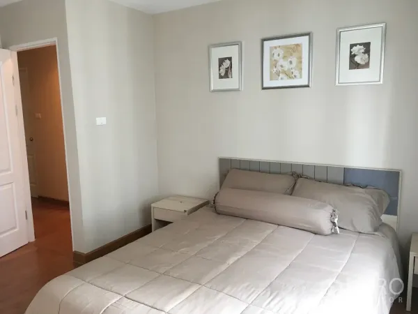 Condominium for rent in Huai Khwang, Bangkok - Bright bedroom with beige bedding, padded headboard and three framed prints on a light wall.