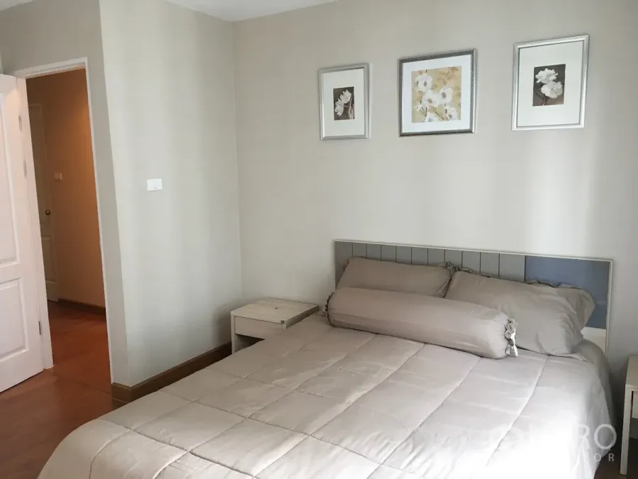 Condominium for rent in Huai Khwang, Bangkok - Bright bedroom with beige bedding, padded headboard and three framed prints on a light wall.