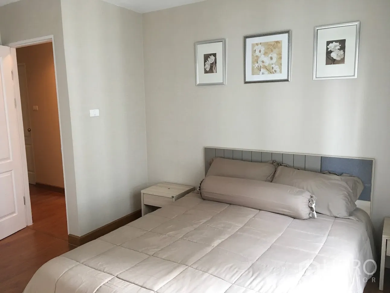 Condominium for rent in Huai Khwang, Bangkok - Bright bedroom with beige bedding, padded headboard and three framed prints on a light wall.